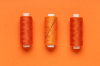 Turuncu zemin üzerinde iğne olan iplik makaraları