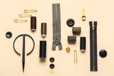 Bej arkaplanda iplik makaraları, fermuarlar, iğneler ve düğmeler ile kompozisyon