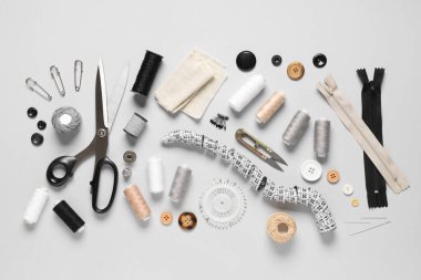 Kumaş, mezura, makas ve gri arkaplandaki dikiş malzemelerinden oluşan iplik makaraları.