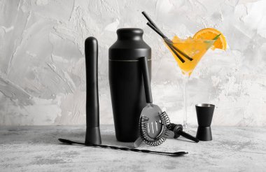 Gri grunge arka planında bir bardak kokteyl olan farklı barmen aletleri.