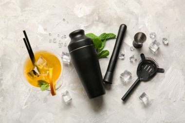 Farklı barmen aletleri, bir bardak kokteyl, nane yaprakları ve hafif grunge arka planda buz küpleri.