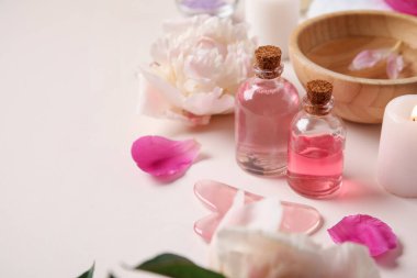 Mumlu gerekli yağlar, guasha masaj aleti ve bej arka planda güzel şakayık çiçekleri.
