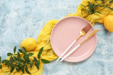 Stylish table setting with plate, cutlery, lemons and leaves on blue grunge background