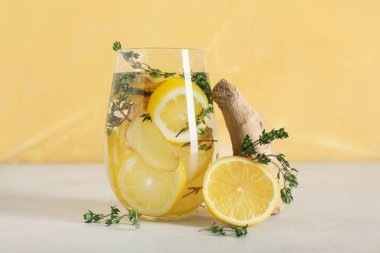 Sarı duvara karşı beyaz masada kekik, zencefil ve limon dilimleri ile doldurulmuş bir bardak su
