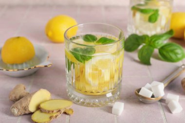 Fesleğen yapraklı, zencefil ve limon dilimli pembe fayanslı bir bardak su.