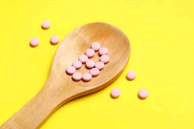 Sarı arka planda pembe vitamin B6 haplı tahta kaşık.