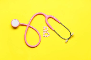 Sarı zemin üzerinde steteskop bulunan pembe B vitamini hapları.