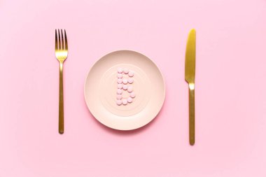 B vitamini haplı tabak ve pembe arka planda çatal bıçak takımı.