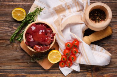 Biberiyeli çiğ ciğer, domates ve ahşap arka planda limon.