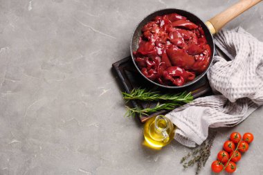 Çiğ ciğer, biberiye, kekik, domates ve gri arka planda bir sürahi yağ ile kızartma tavası.