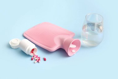 Mavi arka planda haplar ve camlarla dolu sıcak su şişesi.