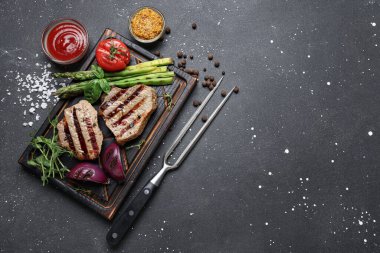 Sebzeli ızgara biftek, ketçap, Dijon hardalı ve siyah grunge arka planda çatal.