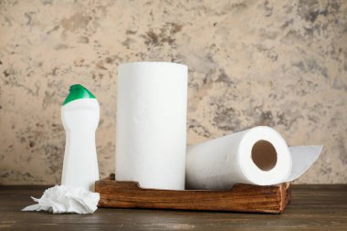 Bej grunge duvarına karşı ahşap masada deterjanlı kağıt havlu ruloları.