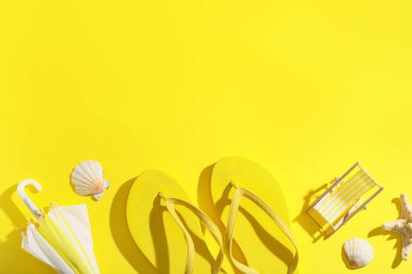 Sarı arka planda deniz kabukları, şemsiye ve şezlonga sahip parlak parmak arası terlikler