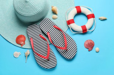 Deniz kabuklu çizgili terlikler, hasır şapka ve mavi arka planda can simidi.