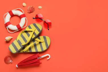 Kırmızı zemin üzerinde deniz kabuğu, güneş gözlüğü, şemsiye ve can simidi olan çizgili parmak arası terlikler.