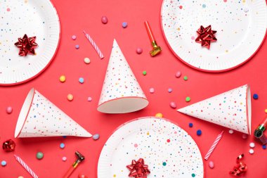 Kırmızı zemin üzerinde tabak, düdük, şeker, mum ve ponpon topları olan koni parti şapkaları