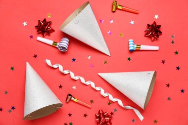 Kırmızı arka planda düdük, yılan ve konfeti olan gümüş parti şapkaları.