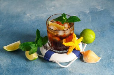 Oyuncak halka şamandıralı, deniz yıldızı ve mavi grunge arkaplanlı soğuk Küba Libre kokteyli.