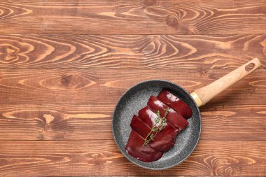 Çiğ ciğer ve ahşap arka planda kekik ile kızartma tavası.