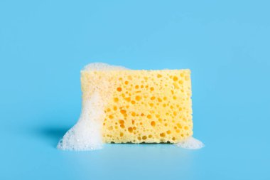 Mavi arka planda köpüklü sarı temizlik süngeri