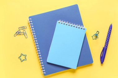 Sarı zemin üzerinde kalem, klasör ve ataç bulunan defterler