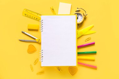 Sarı zemin üzerinde alarm saati ve kırtasiye malzemesi olan defter