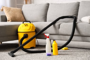 Salondaki halının üzerinde temizlik malzemeleri ve modern elektrikli süpürge var.