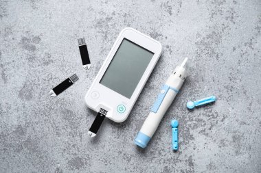 Gri grunge arkaplan üzerinde neşter ve test şeritleri ile glukometre