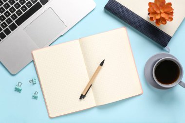 Dizüstü bilgisayarlı defterler, klasör klipleri ve mavi arka planda bir fincan kahve.