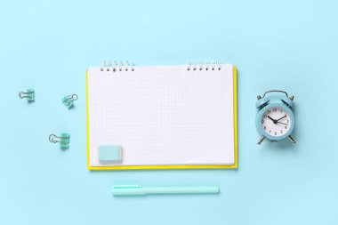 Alarmlı saat, klasör klipleri, silgi ve mavi arkaplan üzerine kalem içeren defter