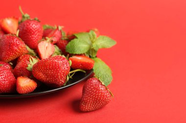 Tatlı çilekli tabak ve kırmızı arka planda yapraklar.