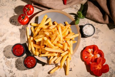 Patates kızartması tabağı, ketçap kaseleri, domates ve bej grunge arkaplanda dolma biber dilimleri.