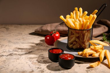 Patates kızartması metal sepette ketçap kaseleri ve bej grunge masasında domatesler.