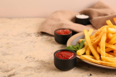 Patates kızartması, fesleğen yaprağı ve bej grunge masasında bir kase ketçap.