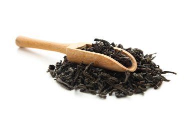 Beyaz arka planda bir yığın kuru siyah çay yapraklı ahşap kepçe.