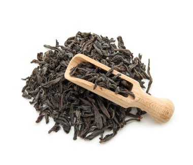 Beyaz arka planda bir yığın kuru siyah çay yapraklı ahşap kepçe.