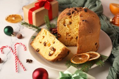 Kesik Panettone tabağı, kurutulmuş portakal dilimleri, köknar dalları ve açık arkaplanda Noel dekoru.