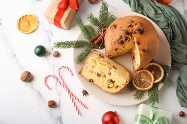 Kesik Panettone tabağı, kurutulmuş portakal dilimleri, köknar dalları ve açık arkaplanda Noel dekoru.