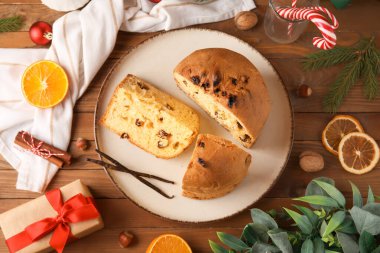 Kesik Panettone tabağı, köknar dalları, baharatlar ve tahta arka planda hediye kutusu.
