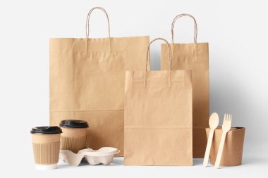 Beyaz arka planda kağıt torbalar, kahve fincanları ve ahşap çatal bıçaklar.
