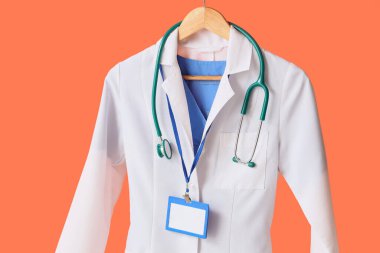 Rozeti olan doktor üniforması ve turuncu arka planda steteskop.