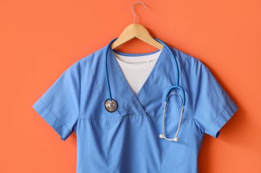 Turuncu arka planda steteskop asılı tıbbi üniforma.