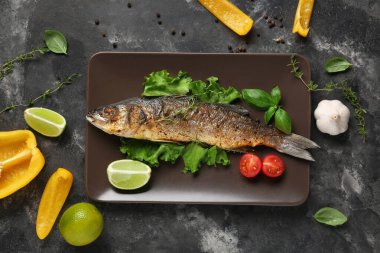 Lezzetli pişmiş deniz kabuğu balığı, marul, otlar, dolmalık biber ve gri grunge arka planda limon dilimleri.