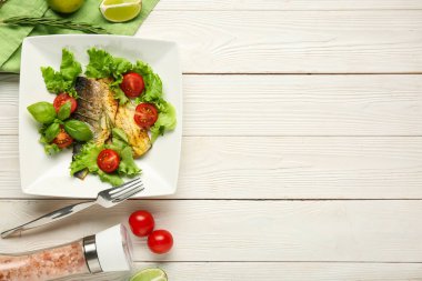 Lezzetli pişmiş deniz kabuğu balığı, marul, otlar, domatesler ve beyaz ahşap arka planda limon dilimleri.