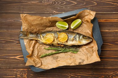 Lezzetli pişmiş deniz kabuğu balığı, biberiye ve ahşap zemin üzerinde limon dilimleri olan fırın tabağı.