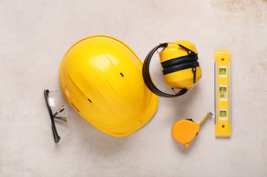 İşitme koruyucuları, güvenlik gözlükleri, ölçüm bandı ve bej grunge arkaplanda ruh seviyesi