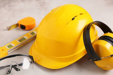 İşitme koruyucuları, güvenlik gözlükleri, ölçüm bandı ve bej grunge arkaplanda ruh seviyesi