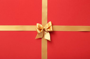 Kırmızı arkaplanda altın saten kurdelelerden yapılmış fiyonk.