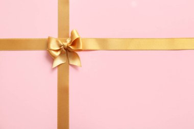 Pembe arka planda altın saten kurdelelerden yapılmış fiyonk.